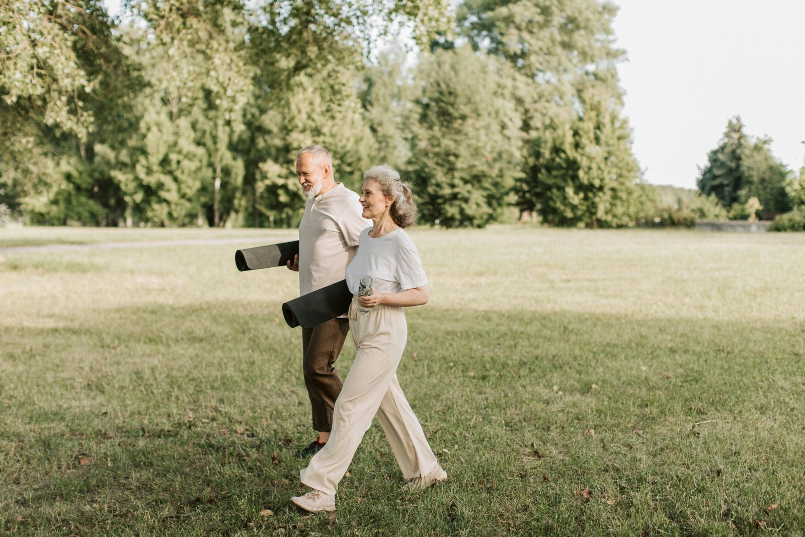 Smiling woman holding a yoga mat near greenery.