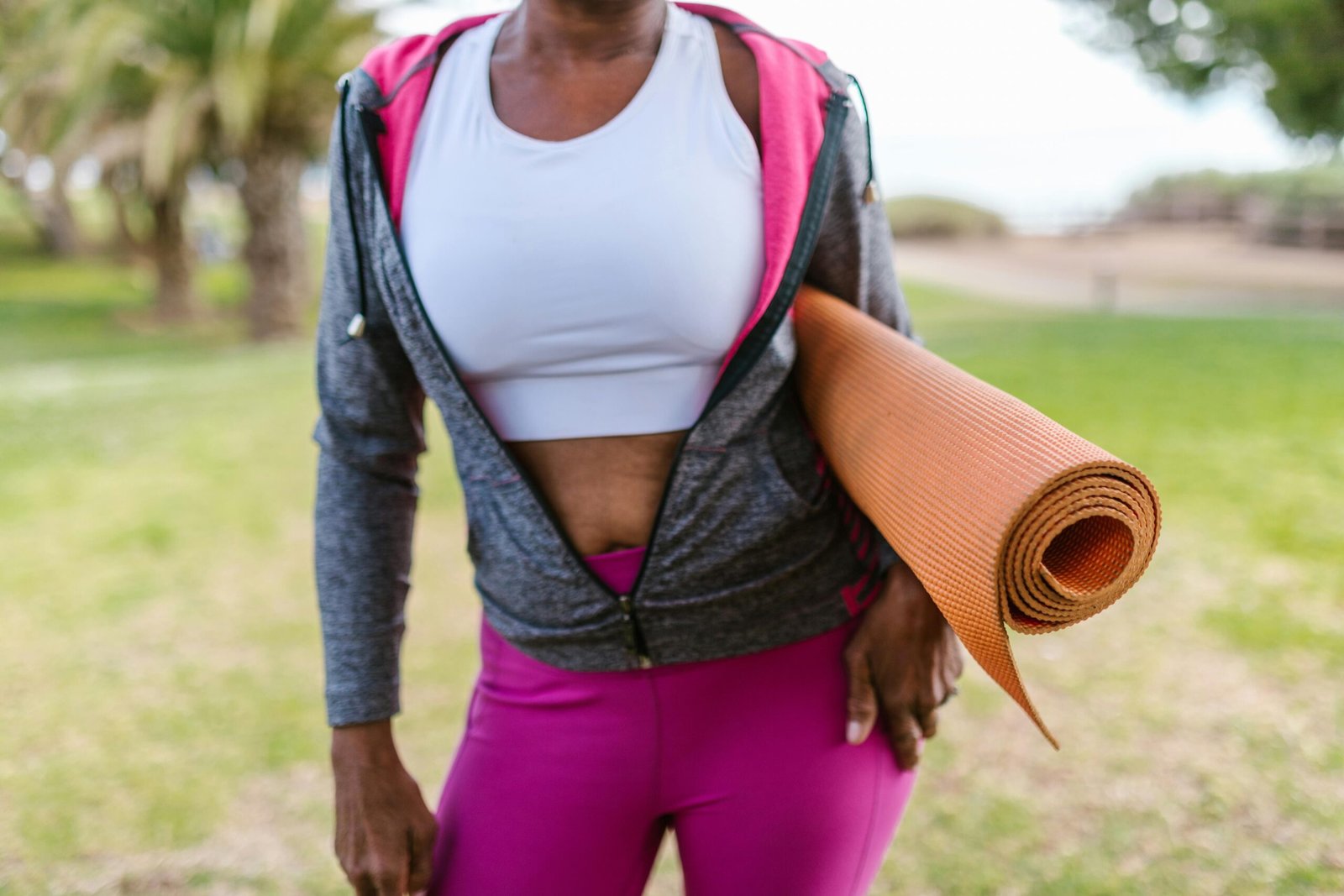Smiling woman holding yoga mat with healthy meal prep containers nearby