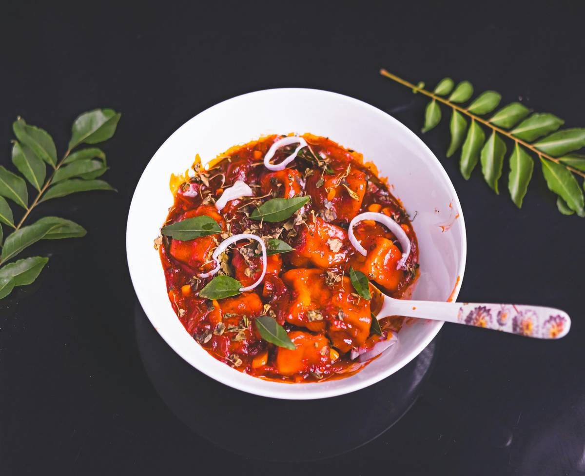A photo of a cozy kitchen counter with spices, vegetables, and a pot of soup steaming